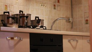 Une cuisine équipée d’une cuisinière, d’un four et d’un évier. On y trouve des placards et un pare-feu en carrelage.