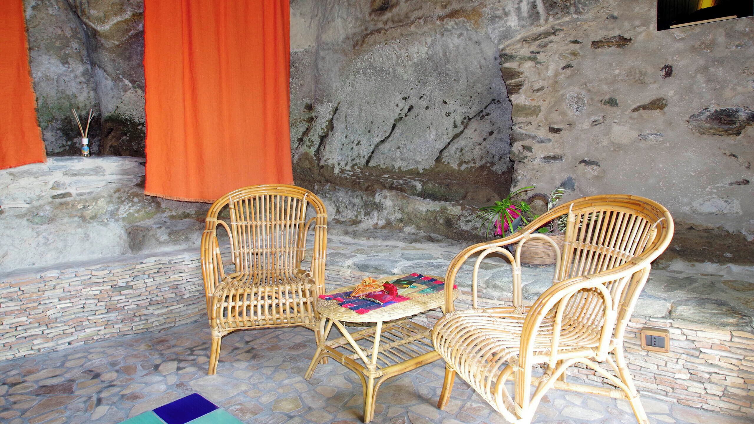 A stone-floored patio with two wicker chairs and a woven table.