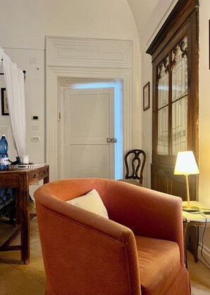 A room with a wooden chair, a table with a water bottle, a lamp, and a door with a light switch.