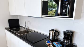 A compact kitchen with a microwave, kettle, and coffee maker on the counter, and a small cabinet above.