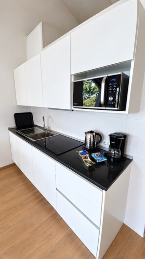 Una cucina compatta con forno a microonde, bollitore e macchina del caffè sul piano di lavoro, e un piccolo pensile sopra.