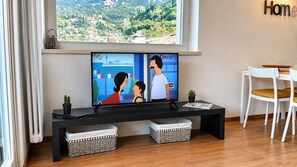 A living room with a large flat-screen TV, a bench, two wicker baskets, and a white chair.