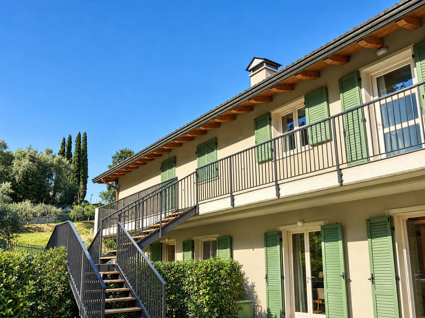 Un bâtiment à deux étages doté d’un balcon, d’un escalier et offrant une vue sur la verdure environnante.