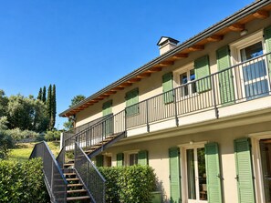 Un edificio di due piani con un balcone, una scala e vista sul verde circostante.