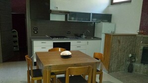 A compact kitchen with white cabinets, a stove, and a sink. There is a wooden dining table with four chairs. - La Tavernetta Apartment CIN IT077014C201874001 (MATERA)
