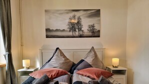 Een slaapkamer met twee bedden, elk met een kussen en een opgerolde handdoek. Boven de bedden hangt een schilderij van bomen.