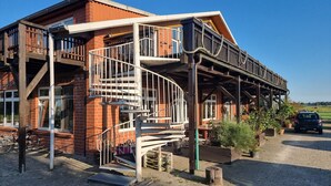 Een huis met twee verdiepingen, voorzien van een houten balkon, een wenteltrap en een grindpad.