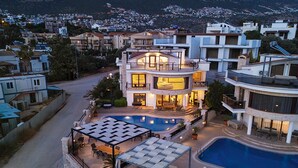 A modern multi-story house with a swimming pool, outdoor seating, and a view of the surrounding neighborhood.