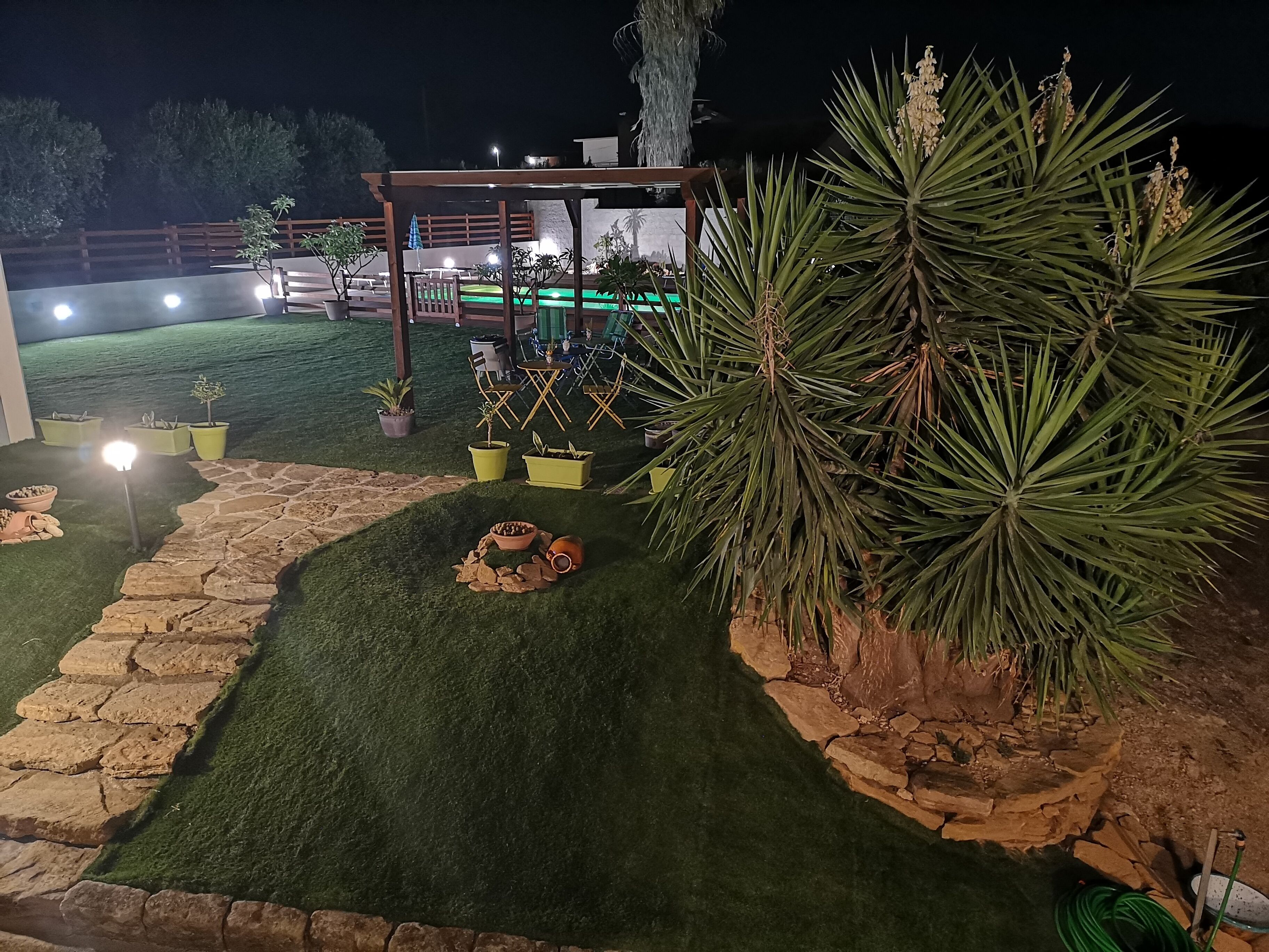 A well-lit outdoor area with artificial grass, potted plants, and a wooden pergola.