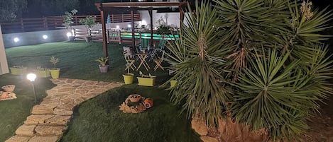 A well-lit outdoor area with artificial grass, potted plants, and a wooden pergola.