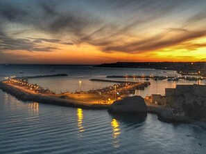 A coastal marina at sunset with calm waters reflecting lights, a pier, and a distant city skyline. - La Rosa Rossa apartment in villa with garden and wonderful panoramic view (Sciacca, Agrigento)