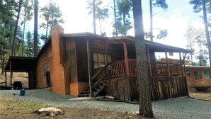 A rustic cabin with a wooden exterior, a covered porch, and a staircase leading to a deck. - Rustic Cabin (Ruidoso)