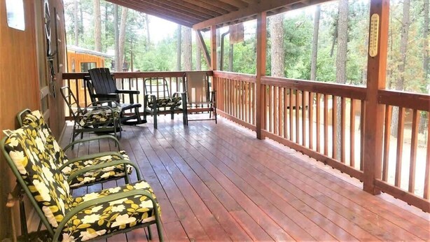 A covered porch with wooden flooring, metal chairs, and a ceiling fan. - Rustic Cabin (Ruidoso)