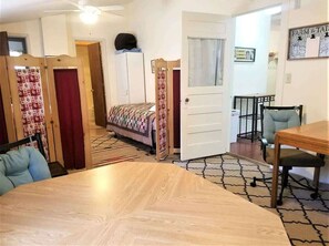 Een kamer met een bed, een eettafel, een stoel, een plafondventilator en een deur.