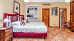 A bedroom with a red and white bed, a bedside table with a lamp, a bookshelf, and a wooden wardrobe.