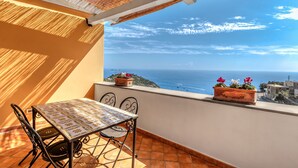 A balcony with a table and chairs, overlooking a scenic view of the sea and a distant coastline.