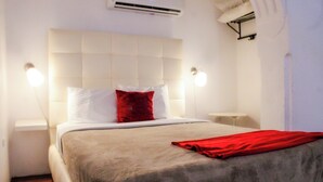 Quarto de hotel com uma cama grande, duas mesas de cabeceira e um cobertor vermelho.