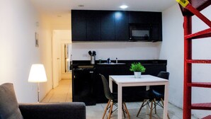 Cozinha compacta com armários pretos, micro-ondas e uma pequena mesa de jantar com duas cadeiras.