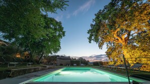 A swimming pool with lounge chairs and a wooden deck, surrounded by trees and a stone building. - IL BORGHETTO Magical property for large groups and families in south Tuscany (saturnia)