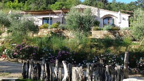 A rustic stone house with a sloped roof, surrounded by lush greenery and flowering plants. - IL BORGHETTO Magical property for large groups and families in south Tuscany (saturnia)