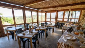 A dining area with wooden tables and chairs, large windows offering a view of the landscape, and a rustic interior design. - IL BORGHETTO Magical property for large groups and families in south Tuscany (saturnia)