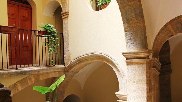 An interior courtyard with stone arches, a wooden door, and a potted plant. - P&G house in historic Sicilian building (Niscemi)