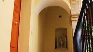 A hallway with a patterned floor, a wooden door, and a statue in the background. - P&G house in historic Sicilian building (Niscemi)