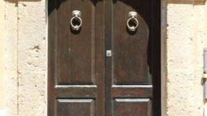 A double wooden door with a stone archway and two round metal knockers. - P&G house in historic Sicilian building (Niscemi)