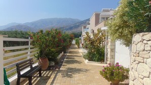 A paved pathway lined with potted plants and a bench, leading to a building with a stone wall and a white fence. - Villa Oniro- Less than 5-Min Walk to Kalivaki Beach with private pool (Chania)