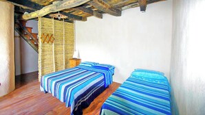 Une pièce avec deux lits, un plancher en bois, un escalier et une tapisserie murale tissée.