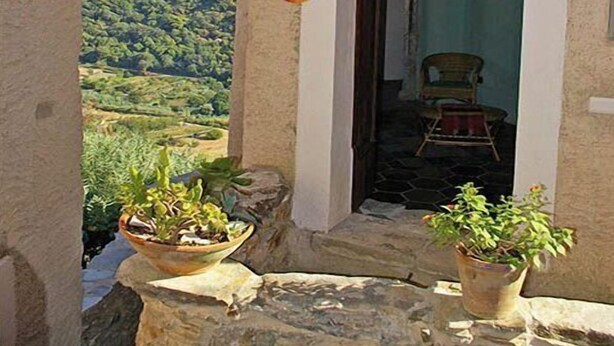 Un bâtiment rustique, doté d’une entrée étroite, d’un mur en pierre et offrant une vue sur une vallée verdoyante.