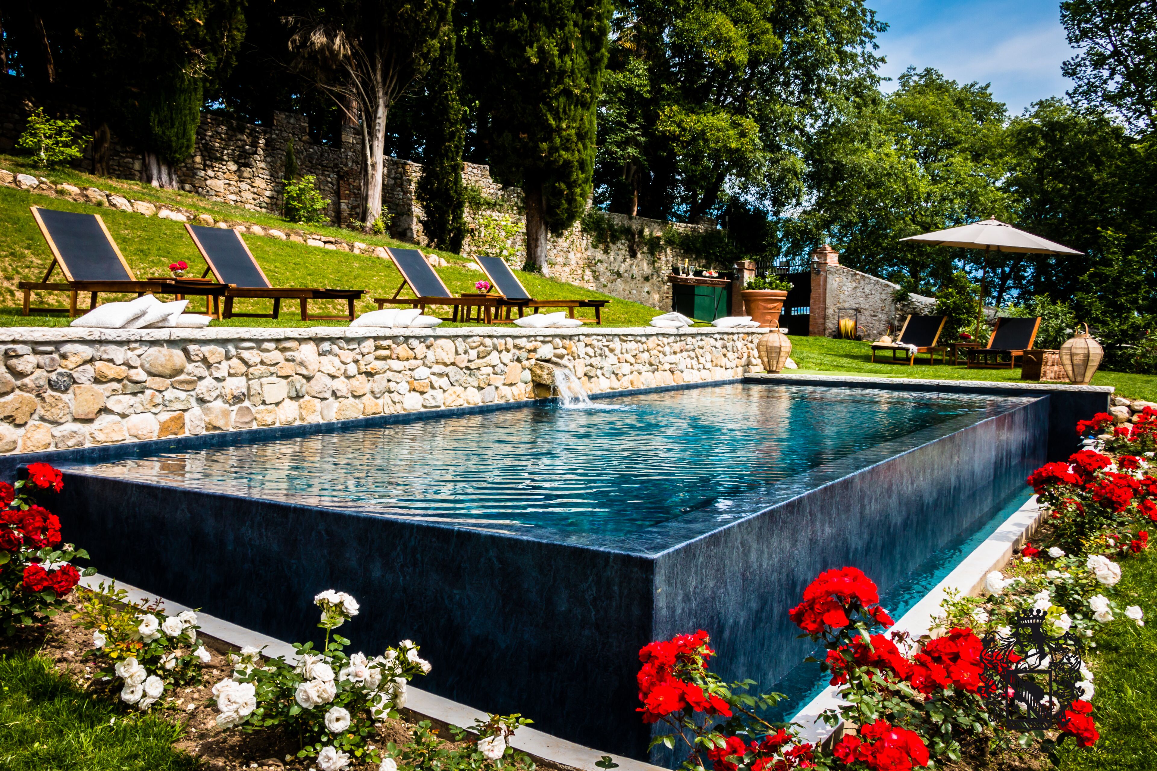 Une piscine rectangulaire entourée d’un mur en pierre, aménagée avec des chaises longues et une petite table.