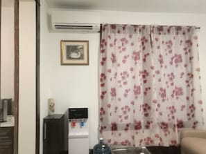 Una habitación con dispensador de agua, un cuadro enmarcado en la pared y una cortina estampada con motivos florales.