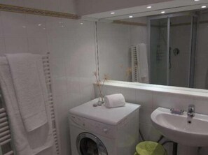 Casa de banho com máquina de lavar roupa, pia e espelho.
