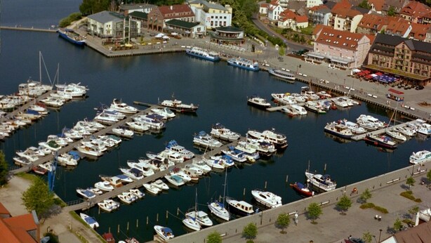 A marina with numerous boats docked, surrounded by buildings and a waterfront promenade.