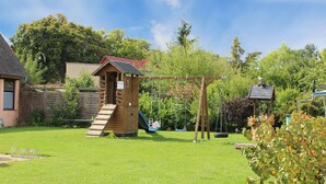 A wooden playhouse with a slide and a swing set in a backyard.