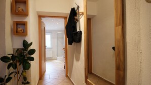 A hallway with a plant, wooden shelves, a coat rack, and a door leading to another room.