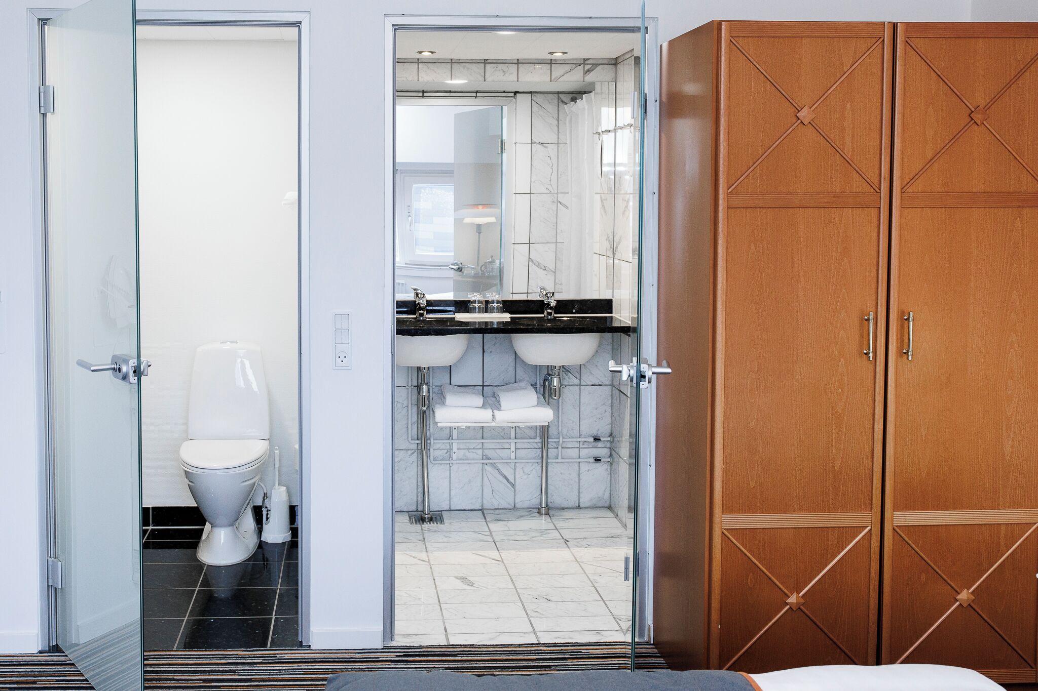 A modern bathroom with a toilet, a glass-enclosed shower, and a vanity with two sinks.
