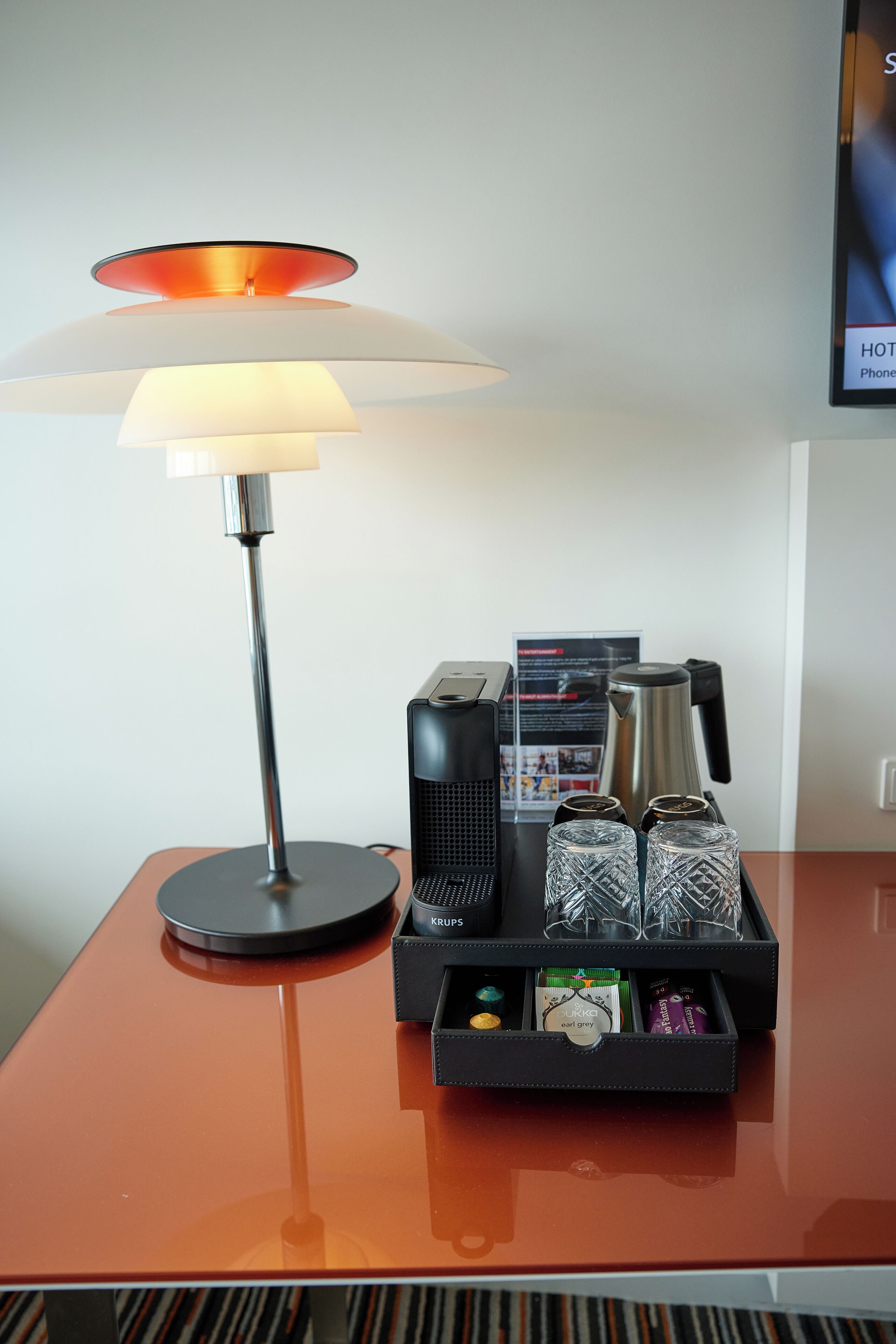 Une chambre d’hôtel équipée d’une lampe moderne, d’une machine à café et d’un plateau contenant divers articles, notamment une bouteille, un verre et une boîte.