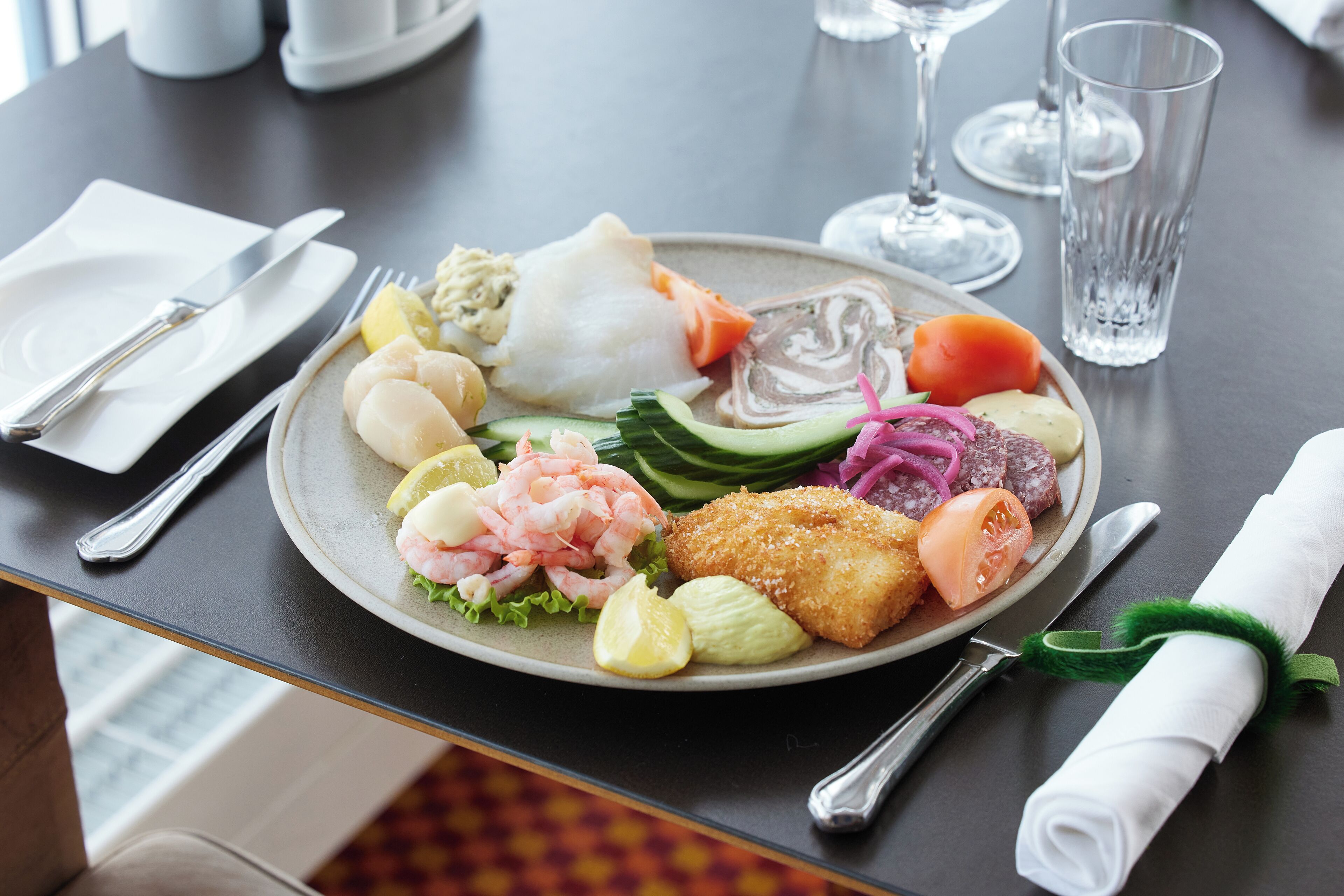 A plate of assorted seafood and vegetables on a table with cutlery and glasses.
