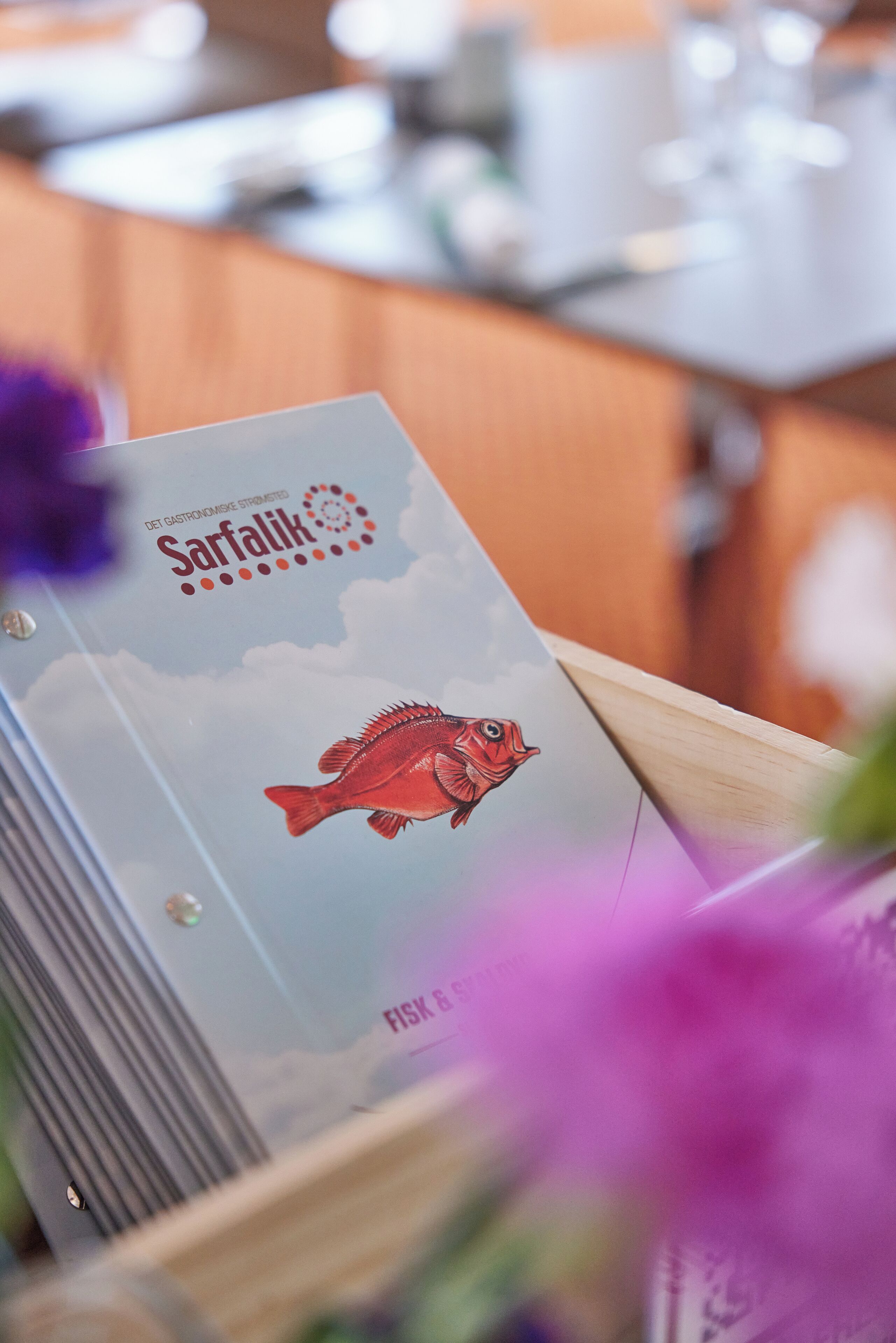 A brochure titled 'Sarfalk' with a fish illustration, placed on a wooden surface with a blurred background.