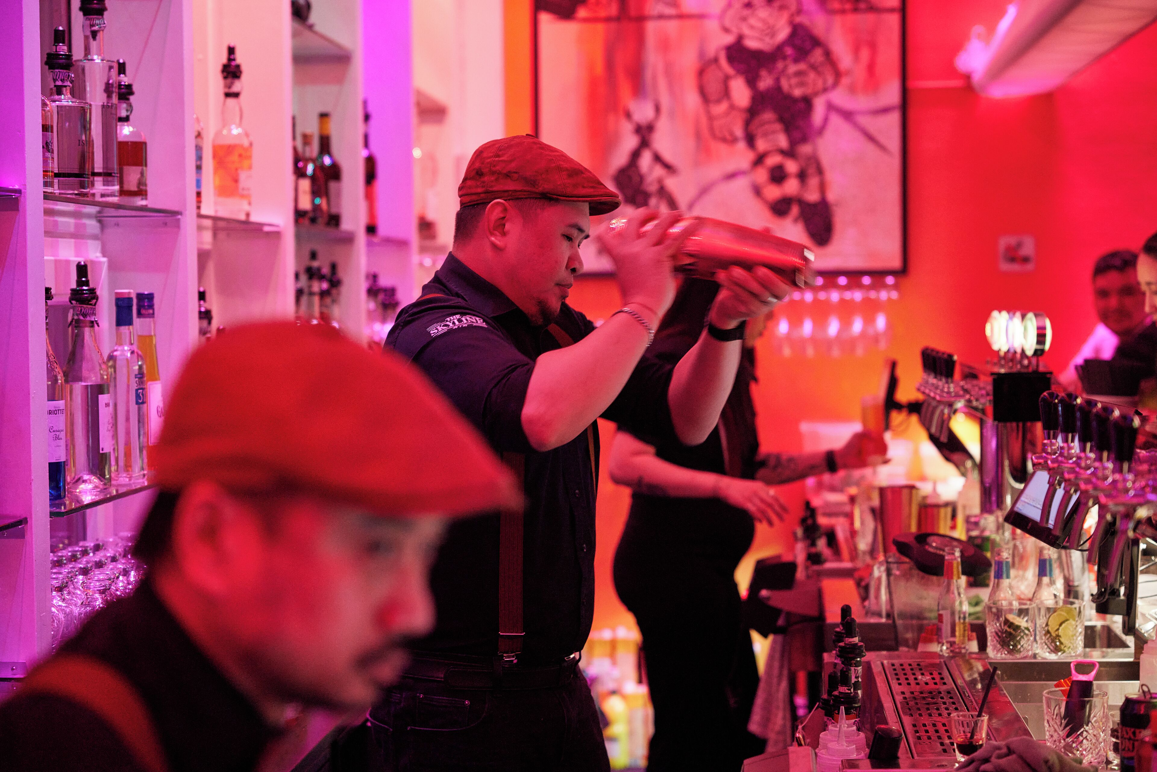 A bar setting with shelves of bottles and a bartender preparing drinks.