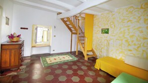 A room with a wooden staircase, a window with curtains, a wooden cabinet with a basket, a patterned rug, and a yellow sofa. - Calabria, Medieval Village, Ecotourism, tradition and culture, sea and nature. (Belmonte Calabro)