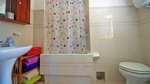 A bathroom with a sink, toilet, shower curtain, and shelves with towels. - Calabria, Medieval Village, Ecotourism, tradition and culture, sea and nature. (Belmonte Calabro)
