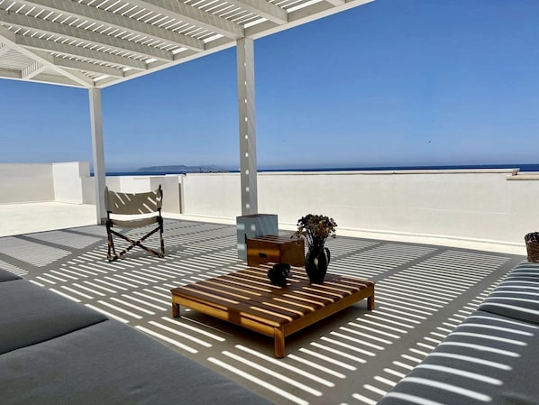 A sunlit outdoor seating area with a wooden bench, a chair, and a small table with a vase of flowers. - Modern Sea View and Beachfront Apartment. (Trapani)