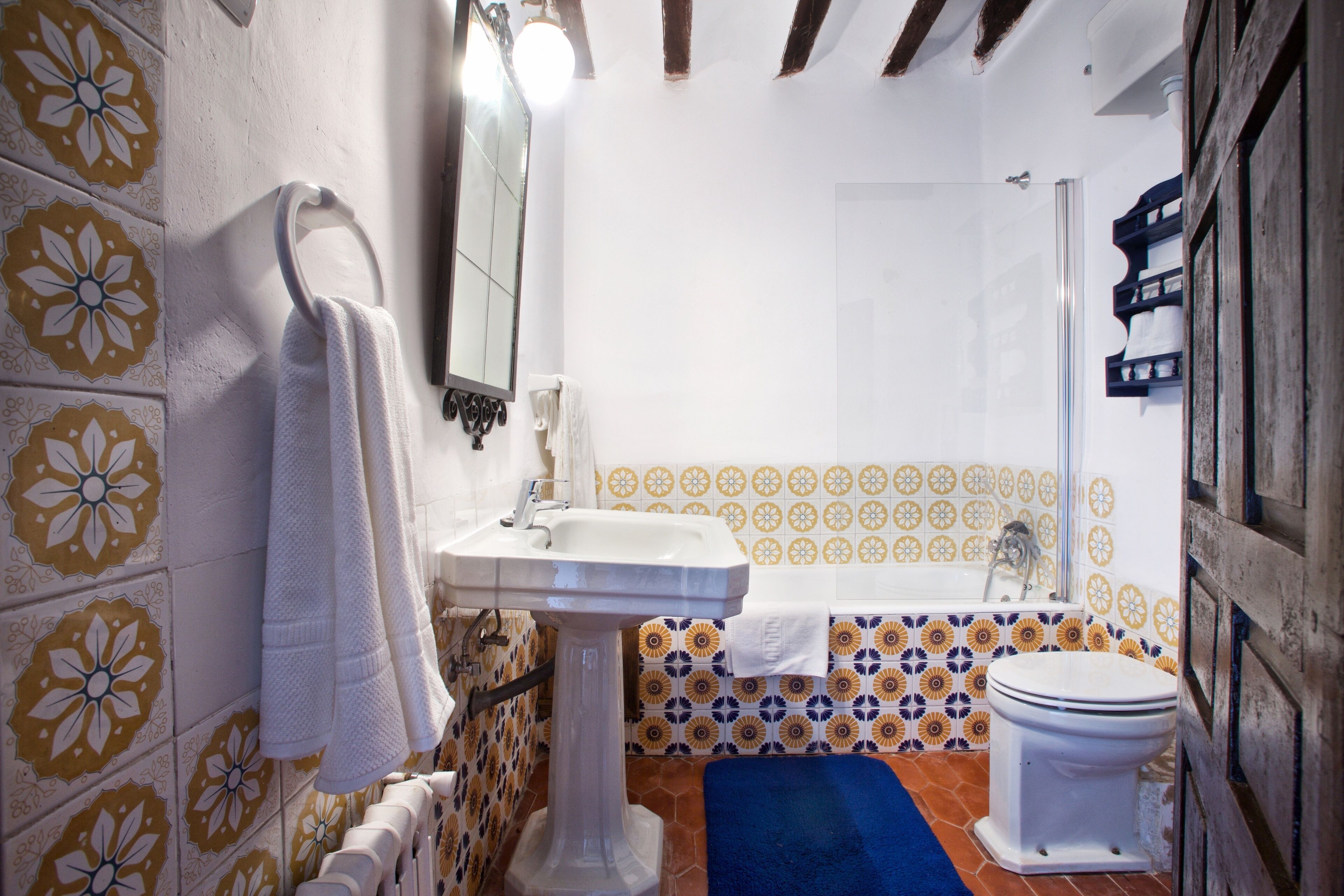 Un bagno con un lavandino su piedistallo, un WC bianco e un tappetino da bagno blu.