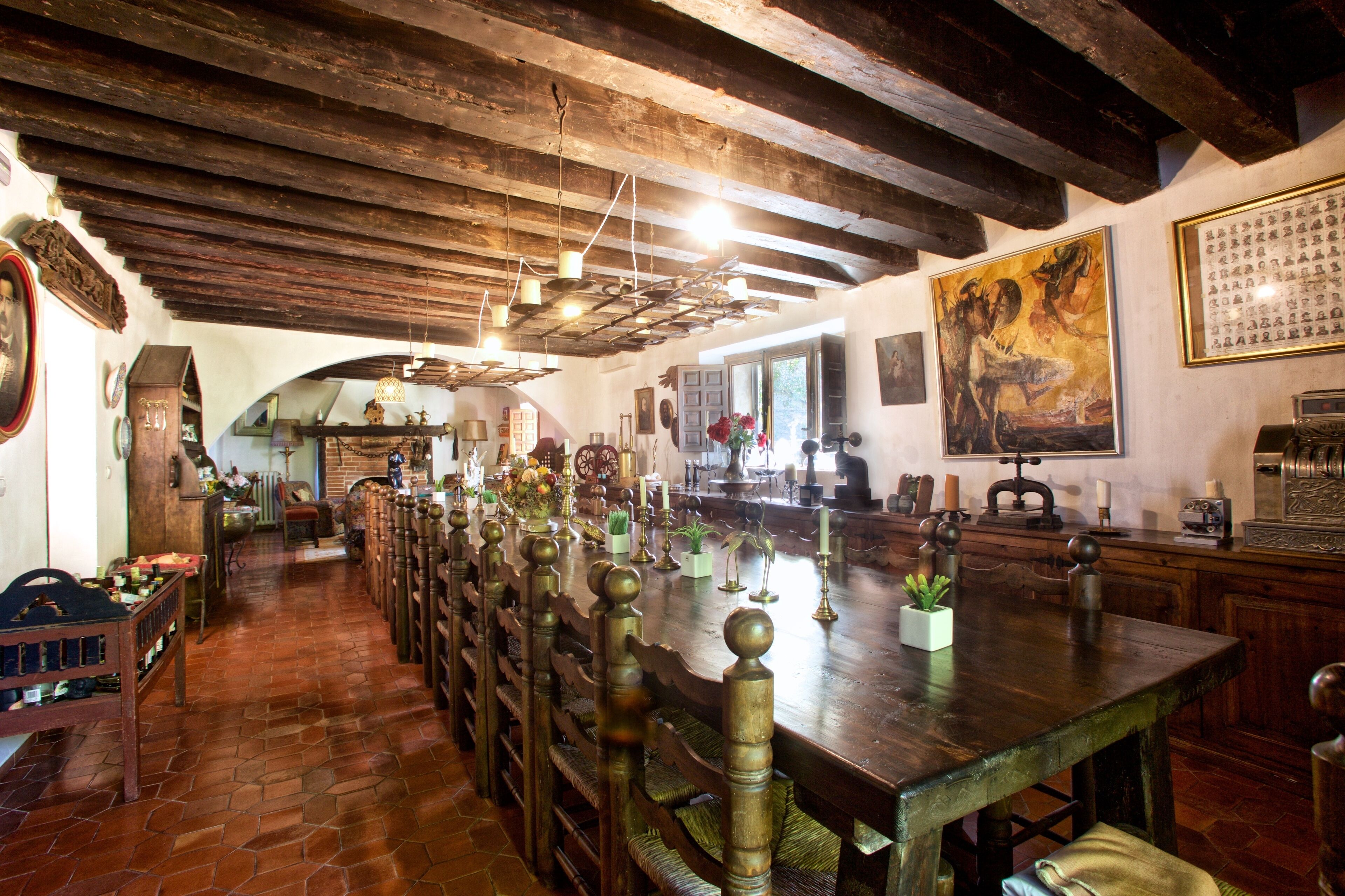 Uma longa mesa de jantar com cadeiras, vigas de madeira e um interior rústico.