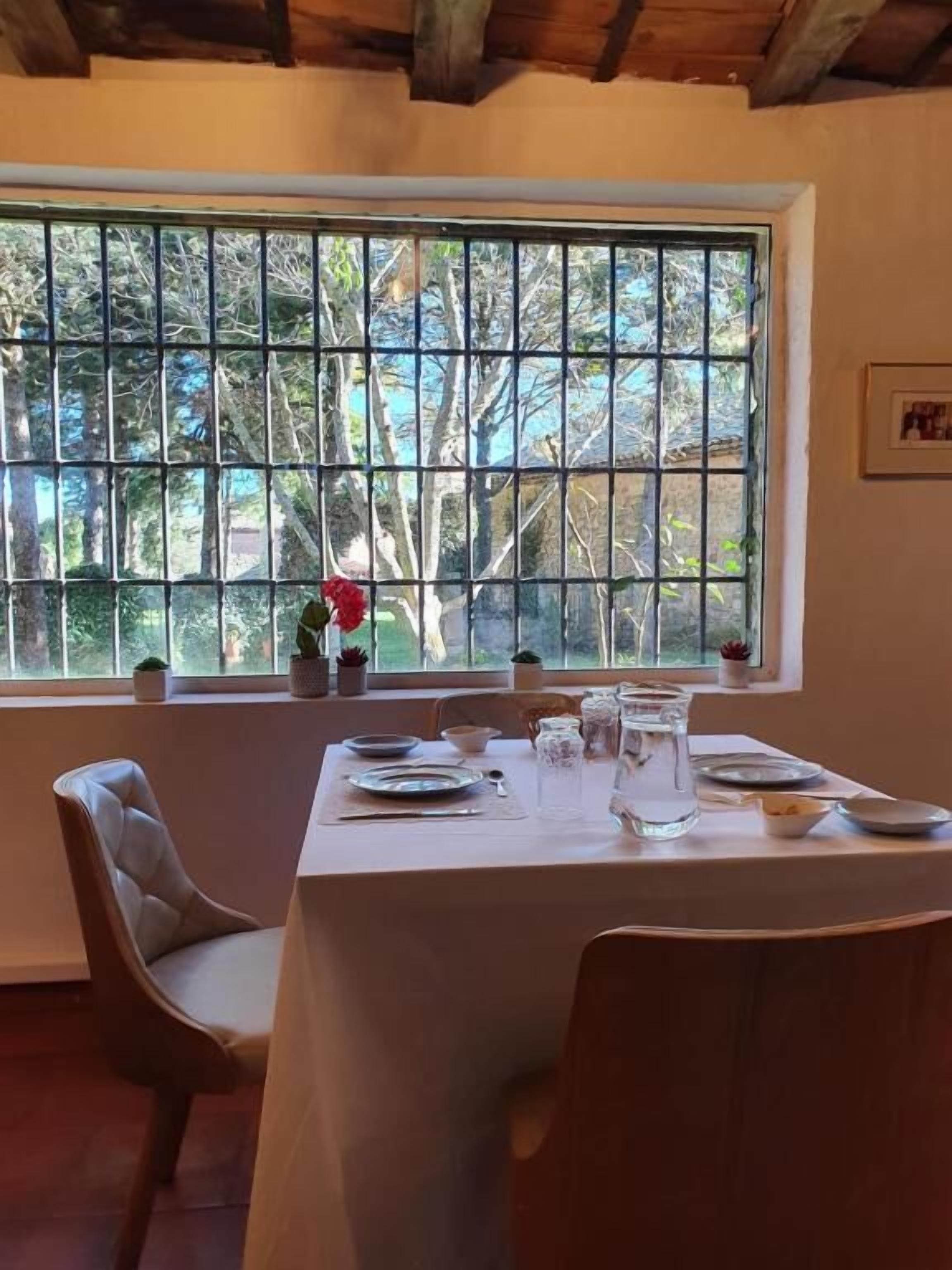A dining area with a table set for two, a window with a view of trees, and a wooden ceiling.