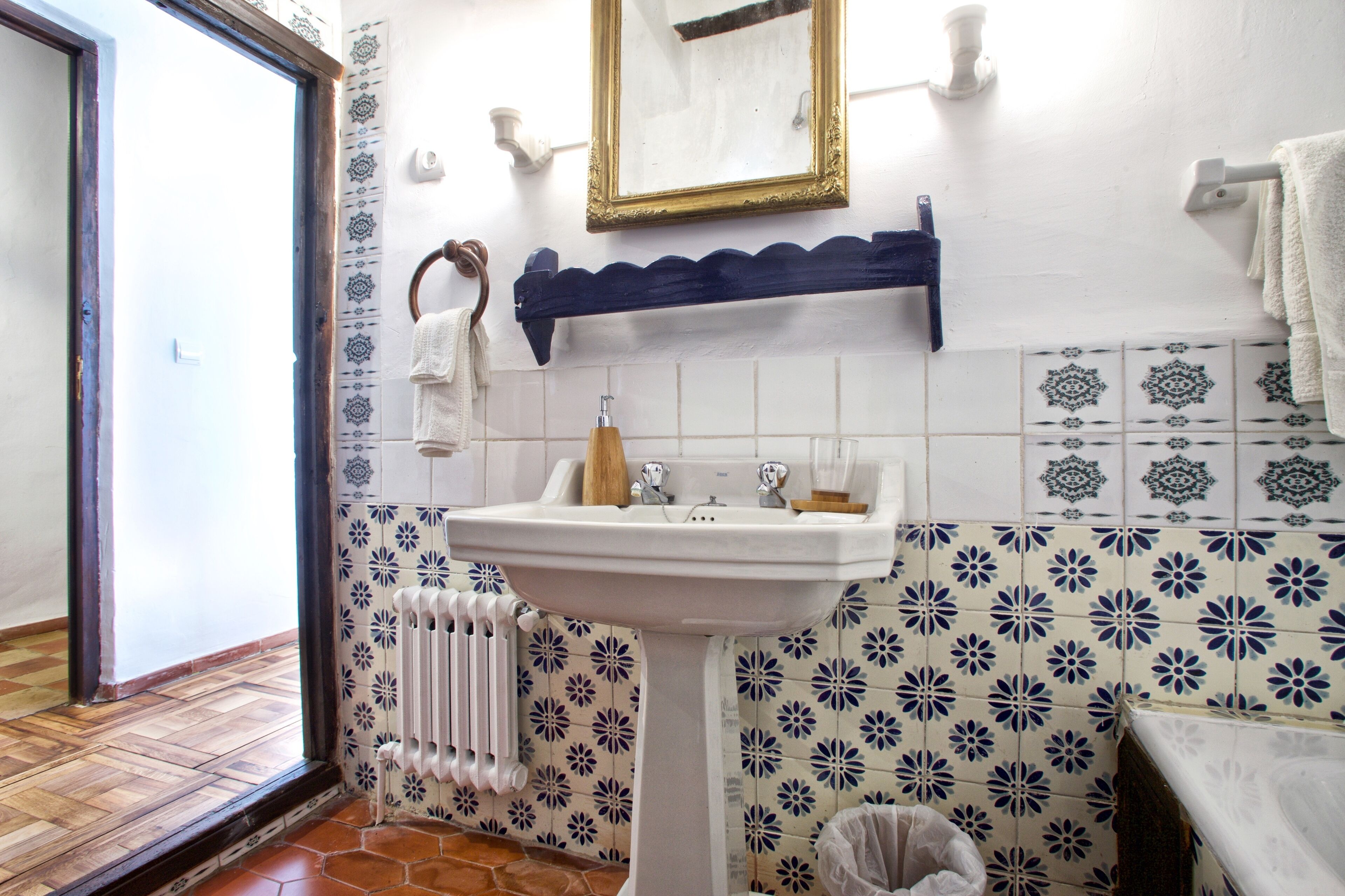 Une salle de bain avec un lavabo blanc, un miroir, un porte-serviettes et des carreaux à motifs.