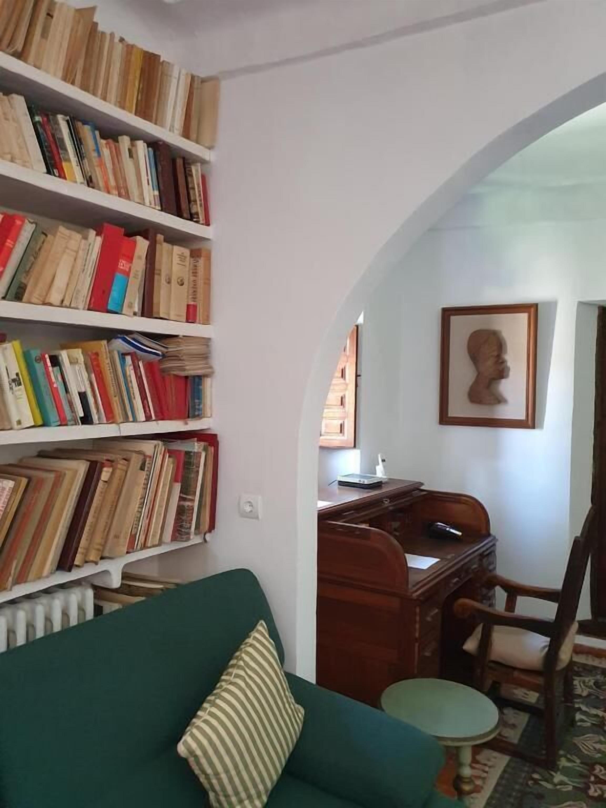 A room with a green sofa, a wooden desk, and a bookshelf filled with books.